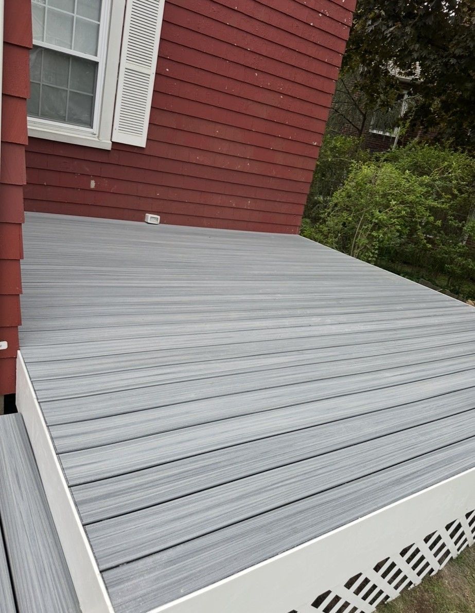 Gray composite deck attached to a red house with white trim and a window.