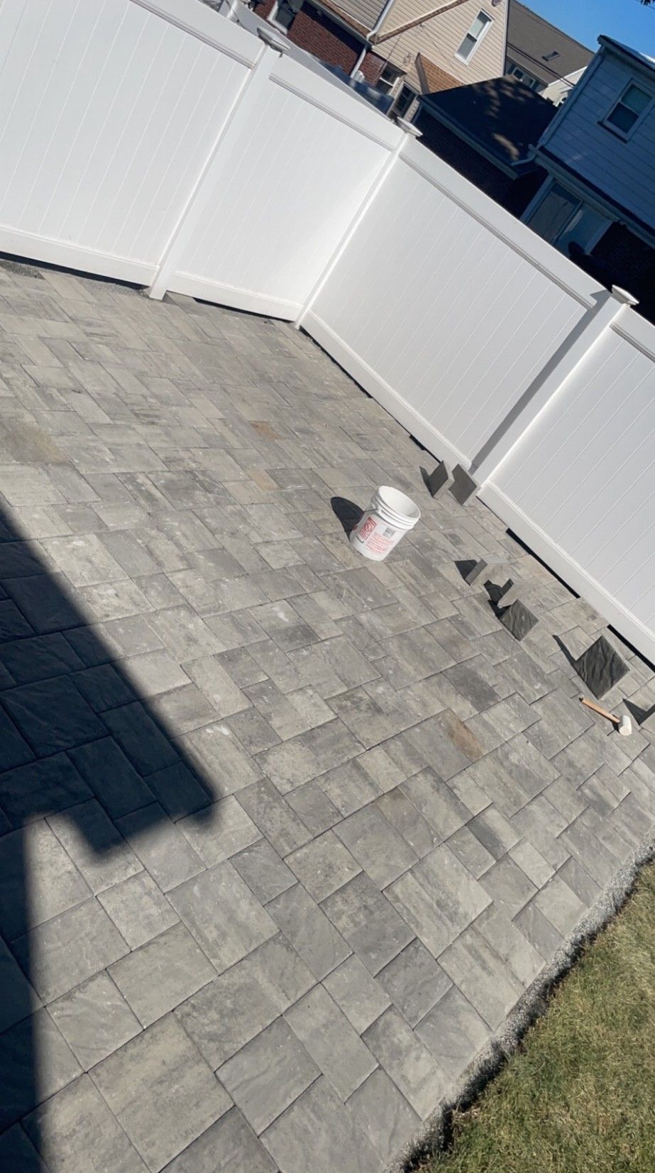 Gray brick patio with white fence in background and grass in the foreground.