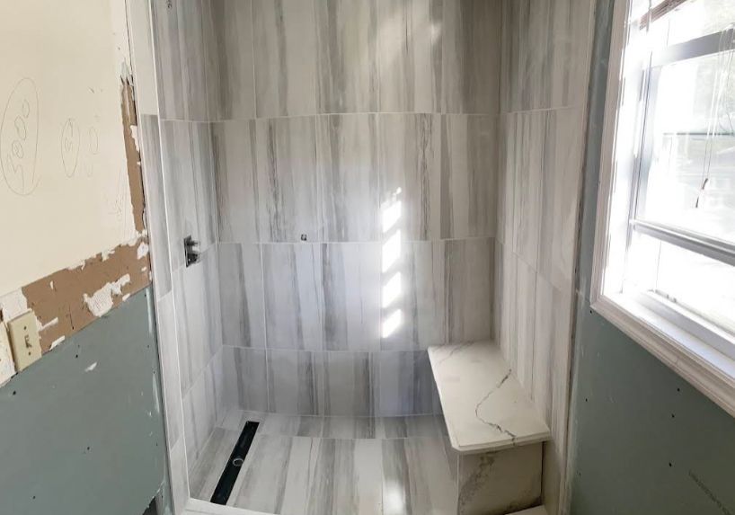 Newly tiled shower with built-in bench, featuring gray and white marble-look tiles.