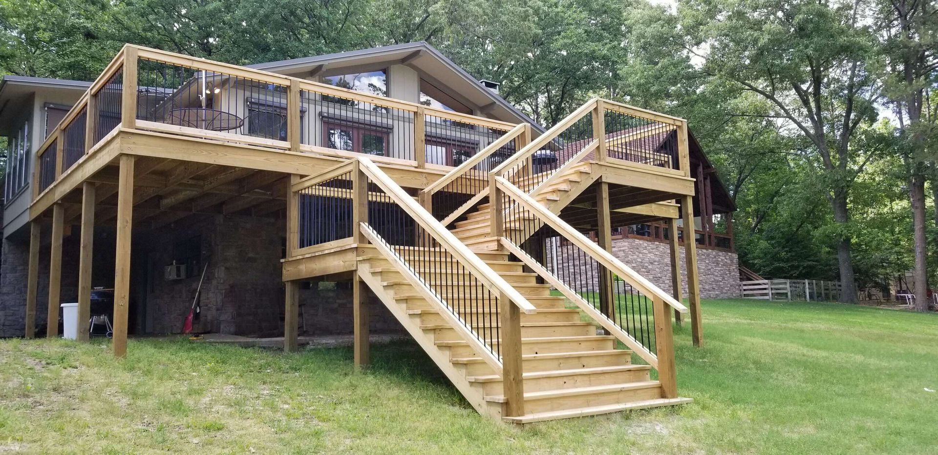 A large wooden deck with stairs leading up to it is in front of a house.