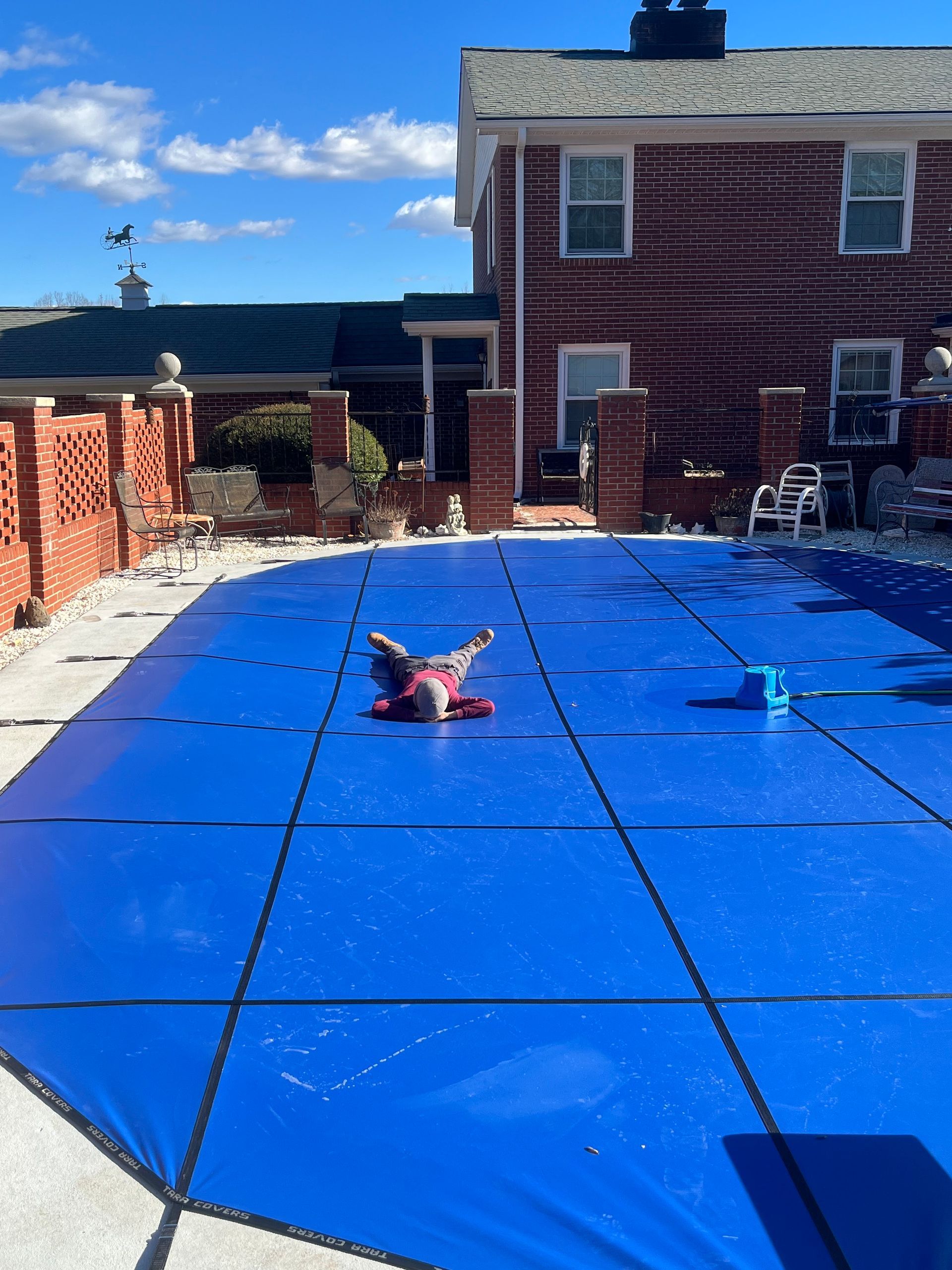 A person is laying on top of a blue pool cover.