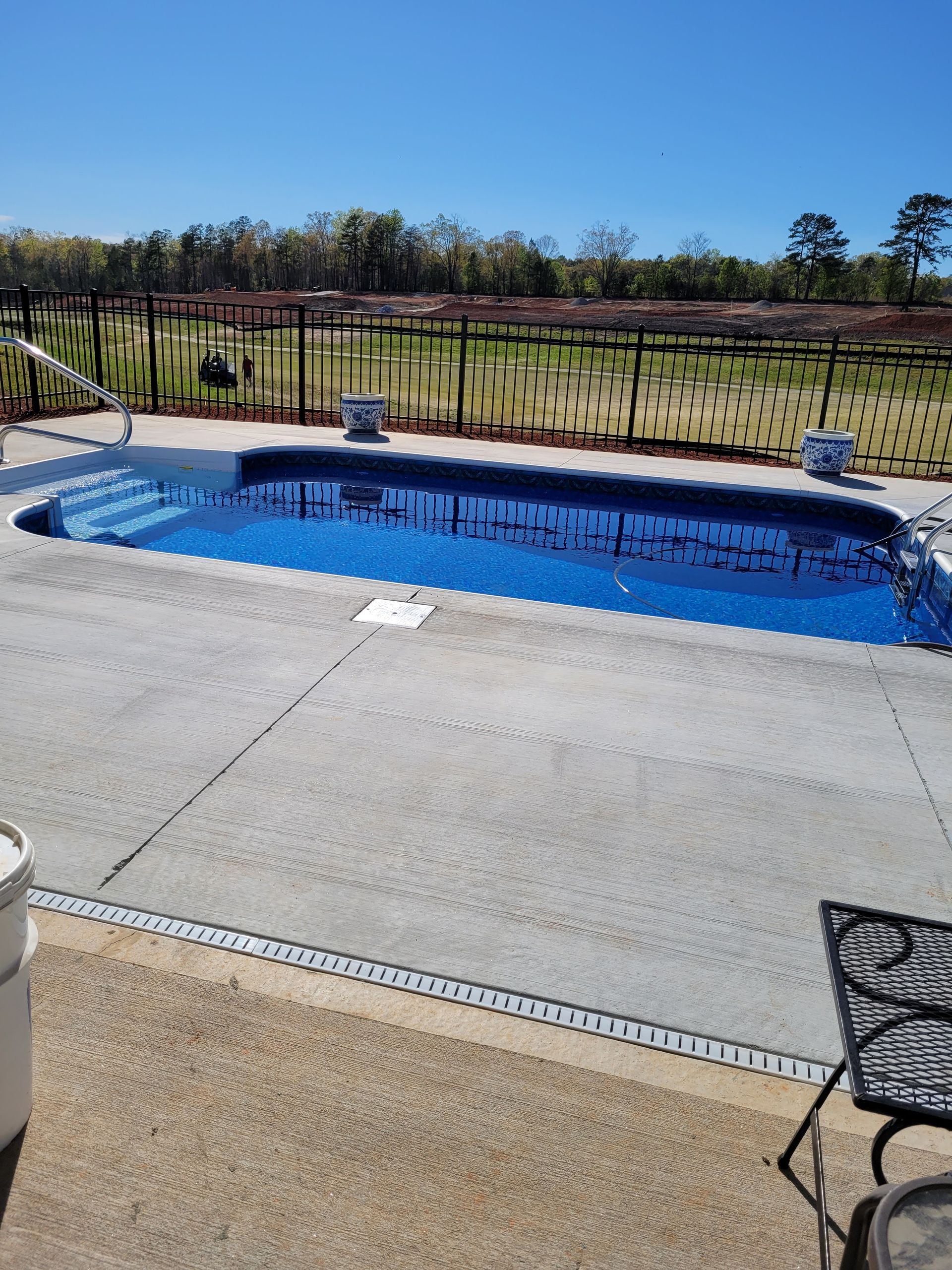 A large swimming pool is surrounded by a fence on a sunny day.