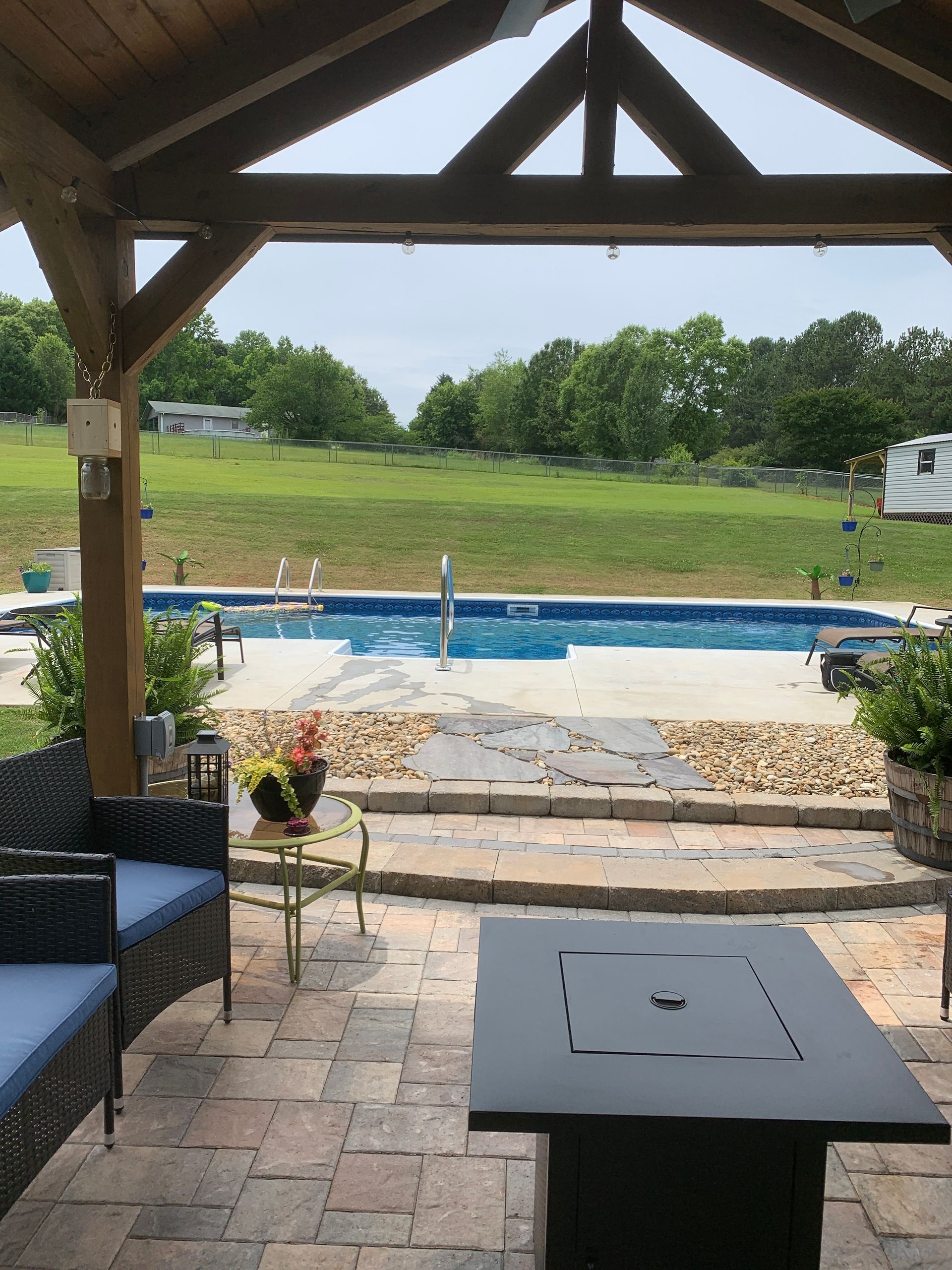 A patio with a fire pit and a swimming pool in the background