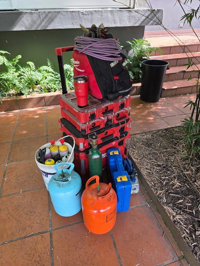 Una pila de cajas de herramientas rojas con tanques de gas y equipos de varios colores en un patio.