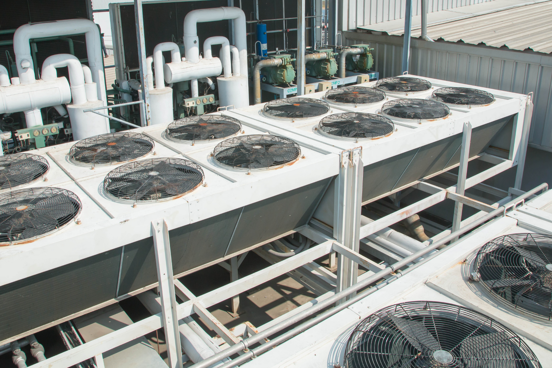 Unidades de aire acondicionado industriales de azotea con múltiples ventiladores y tuberías blancas.