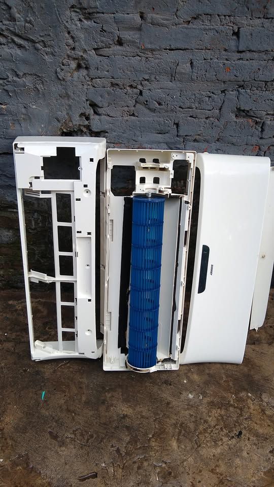 Unidad de aire acondicionado blanca desmontada sobre una superficie oscura, con los componentes expuestos 