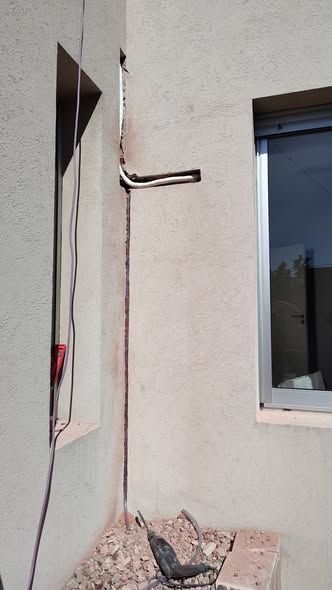 Tubo de cobre montado en una pared de estuco color canela, cerca de una ventana y un espacio de pared vacío.