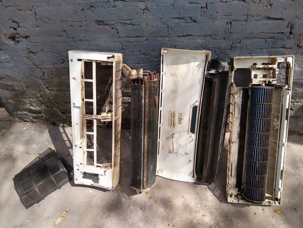 Piezas desmontadas del aire acondicionado colocadas sobre una superficie frente a una pared de ladrillos.