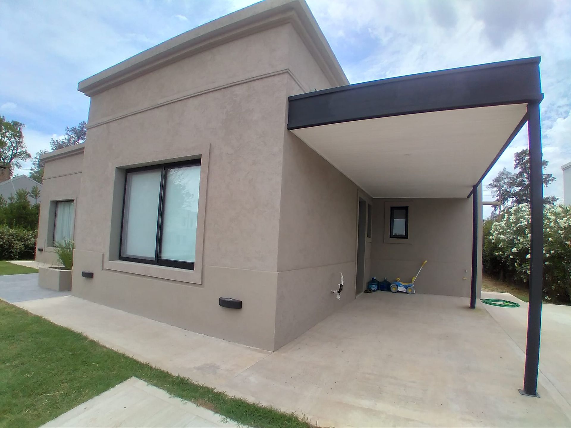 Casa beige con ventanas con marcos negros y cochera. Entrada de hormigón y césped verde.