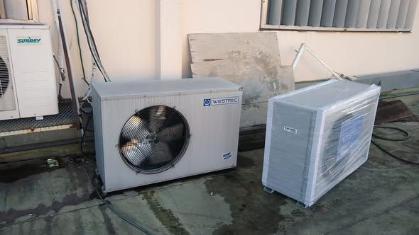Dos aparatos de aire acondicionado en una azotea. Uno con el ventilador a la vista y el otro envuelto en plástico.