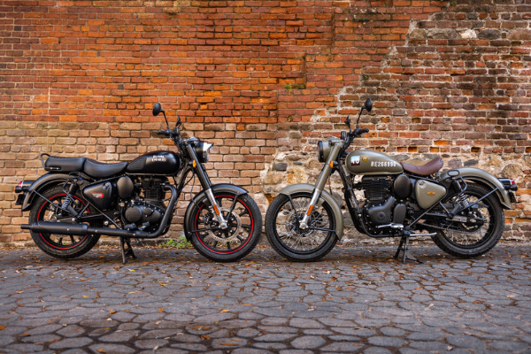 Two black motorcycles parked side by side on cobblestones against a brick wall.