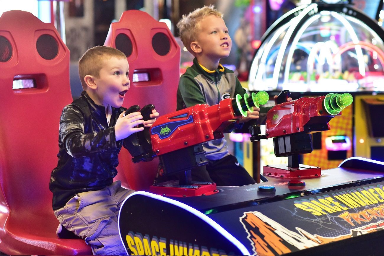 Two young boys are playing a video game in an amusement park.