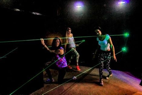 Three women are standing next to each other in a dark room with green lasers.
