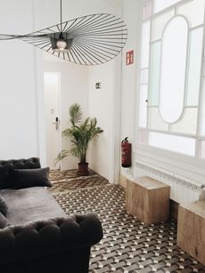Living room with grey sofa, patterned floor, large window, wooden benches, and unique light fixture.
