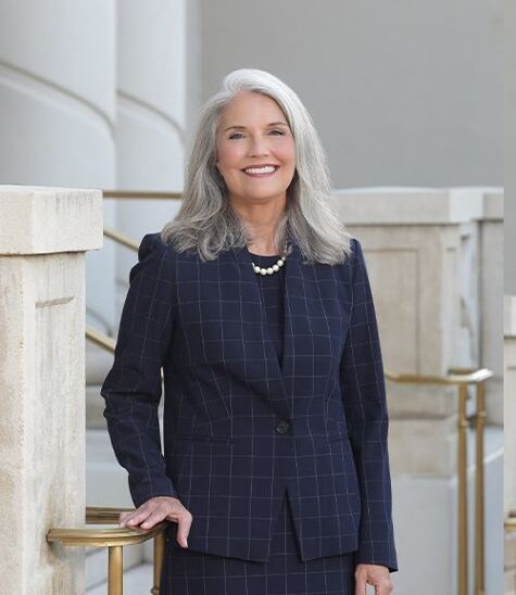 A woman in a blue suit and pearl necklace is smiling