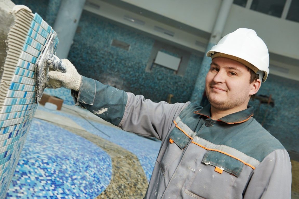 An image of a worker grouting and cleaning tile in a pool.
