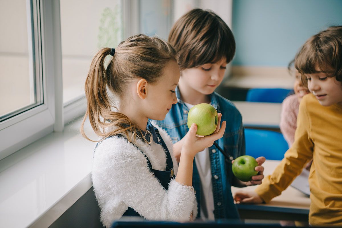Un niño y una niña están oliendo una manzana en un aula.