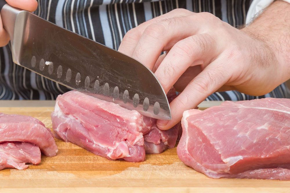 Una persona está cortando un trozo de carne en una tabla de cortar.
