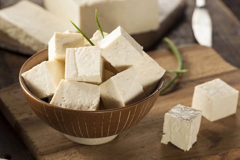Un tazón de cubos de tofu sobre una tabla de cortar de madera.