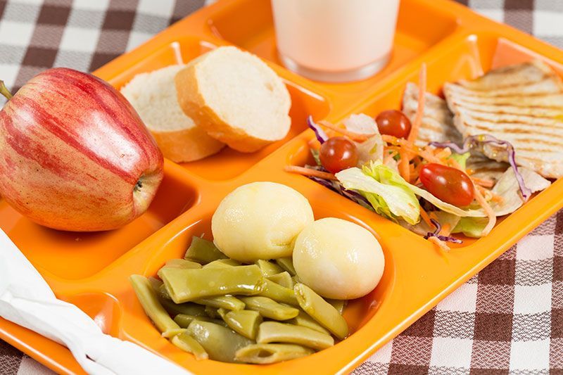 Una bandeja naranja llena de frutas, verduras y un vaso de leche.