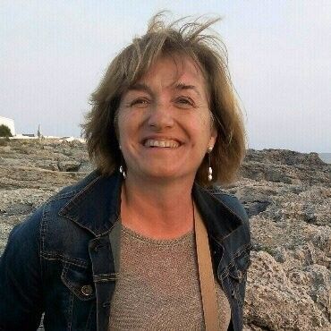 Una mujer con una chaqueta vaquera sonríe mientras está de pie en un acantilado rocoso.