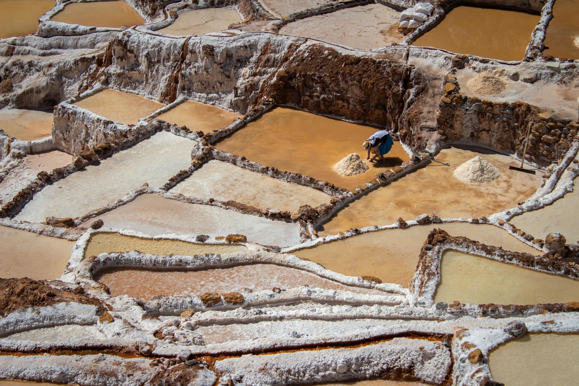 Salt flats with shallow amber pools separated by white mineral ridges; a small blue object sits on one pool edge.