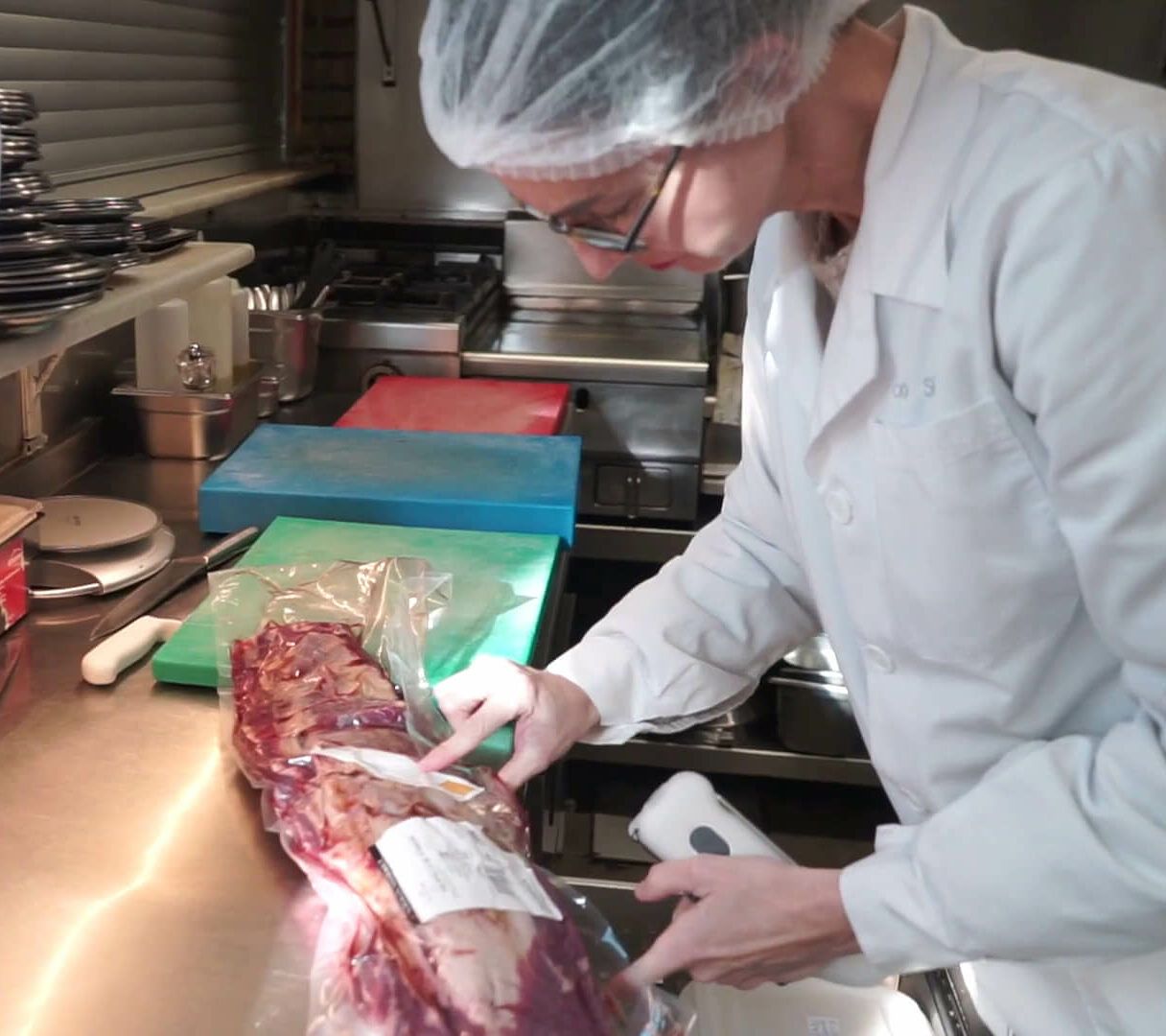 Un hombre con una bata blanca está cortando un trozo de carne.