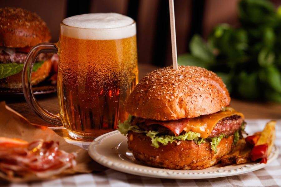Una hamburguesa está en un plato al lado de un vaso de cerveza.
