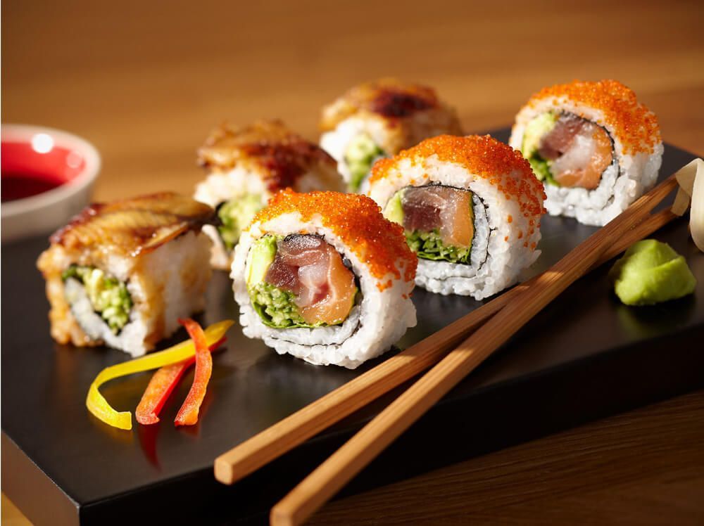 Un plato negro cubierto con rollos de sushi y palillos.