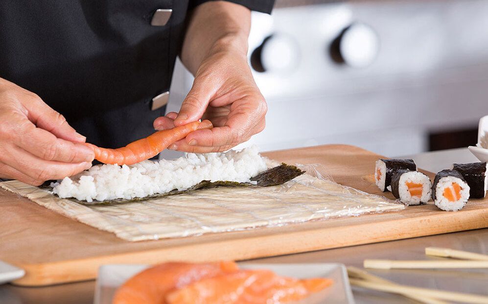 Una persona está haciendo sushi en una tabla de cortar de madera.