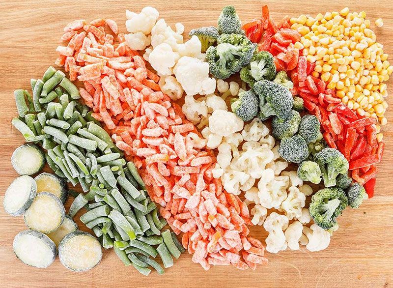 Una tabla de cortar de madera cubierta con una variedad de verduras congeladas.