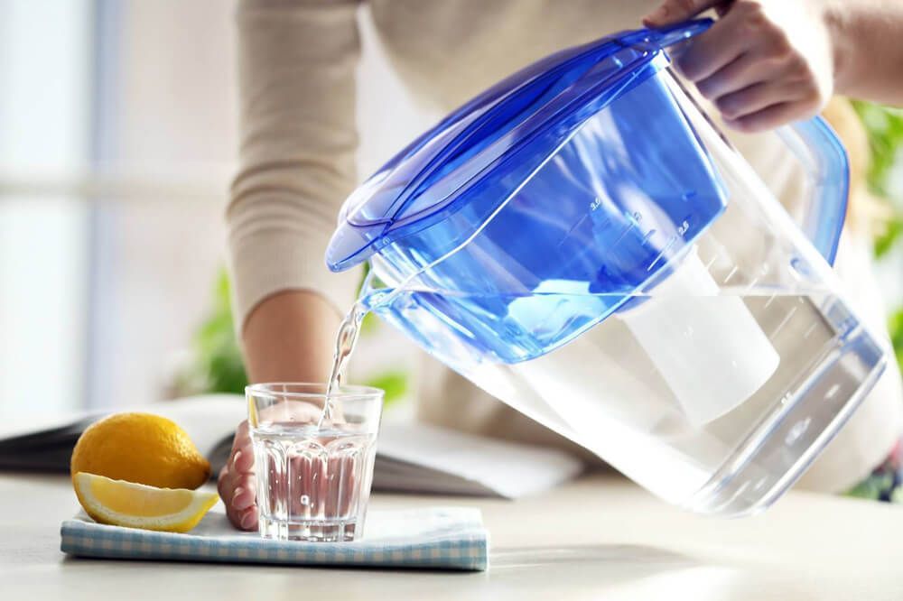 Una mujer está vertiendo agua de una jarra azul en un vaso.