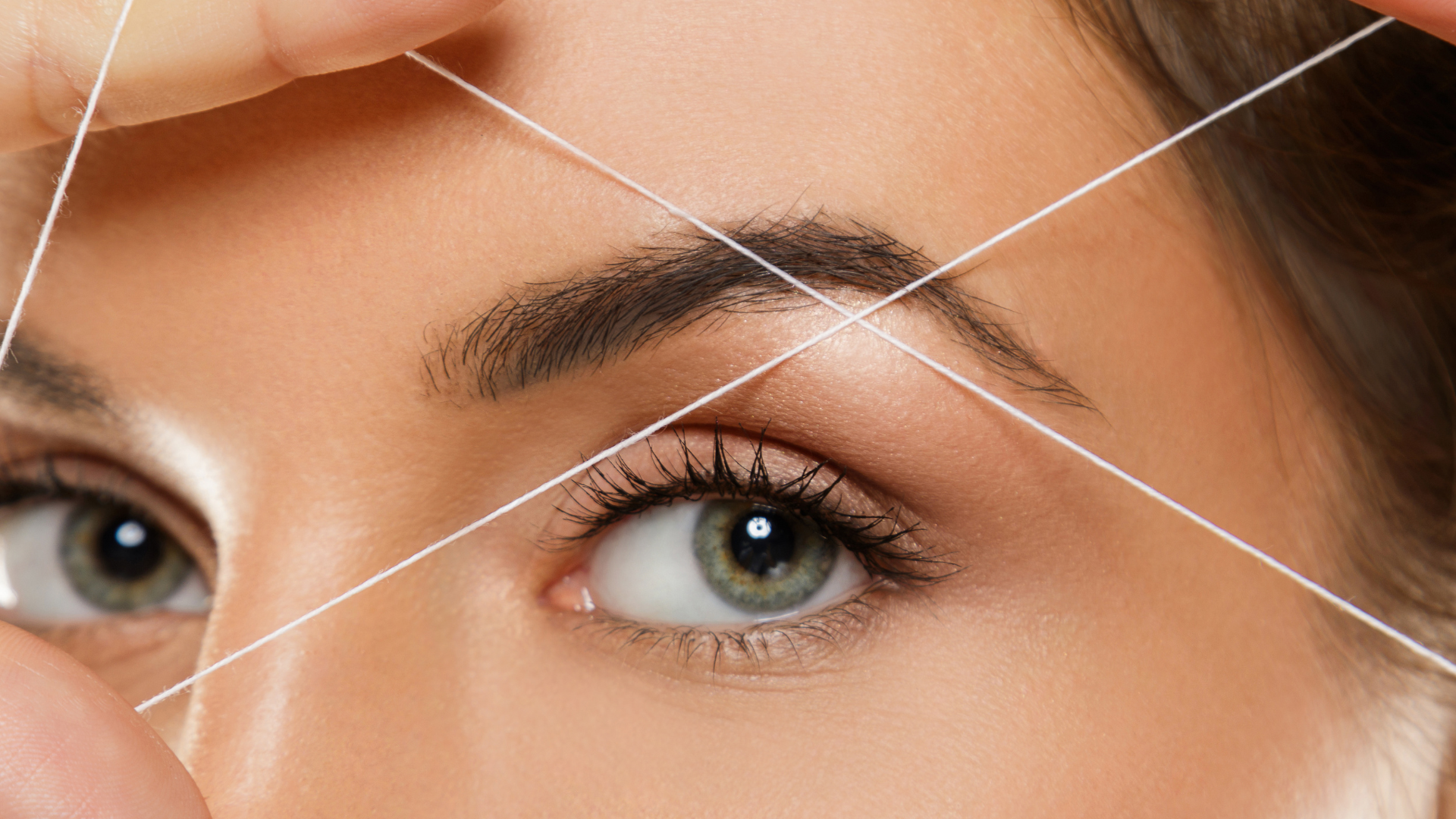 A woman is threading her eyebrows with a string.