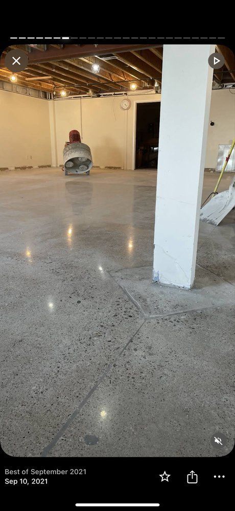 Empty warehouse with polished concrete floor, white pillars, and a person sitting in the distance.