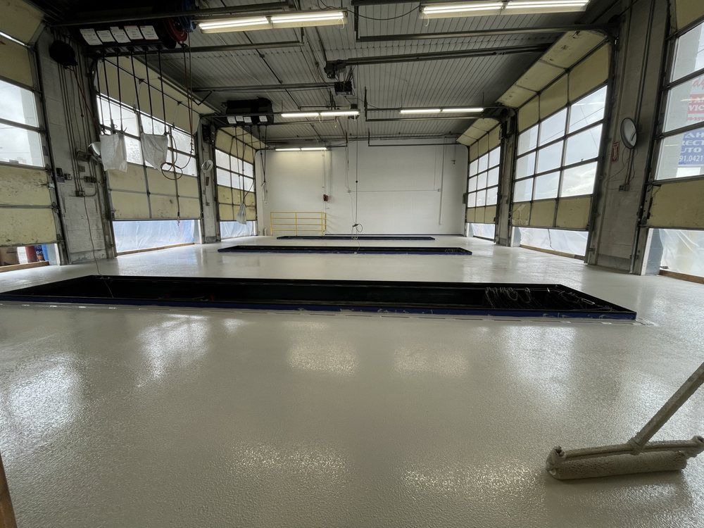 Empty industrial garage interior with a shiny white floor, large windows, and an open floor pit.