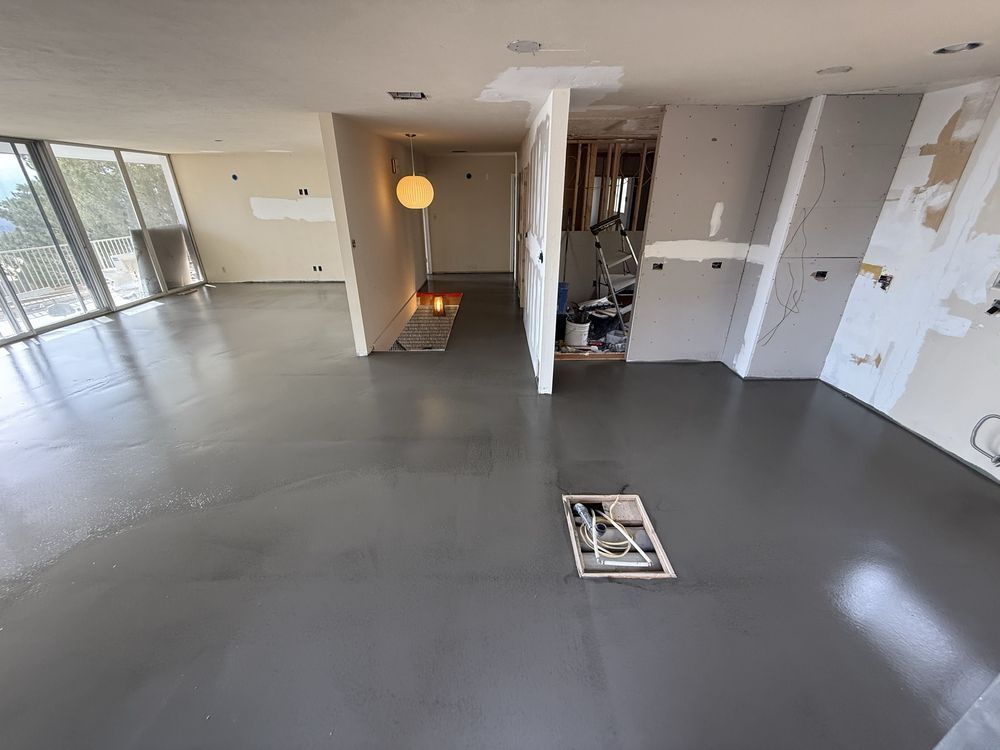 Empty apartment with gray floors, open kitchen area, and large windows letting in natural light
