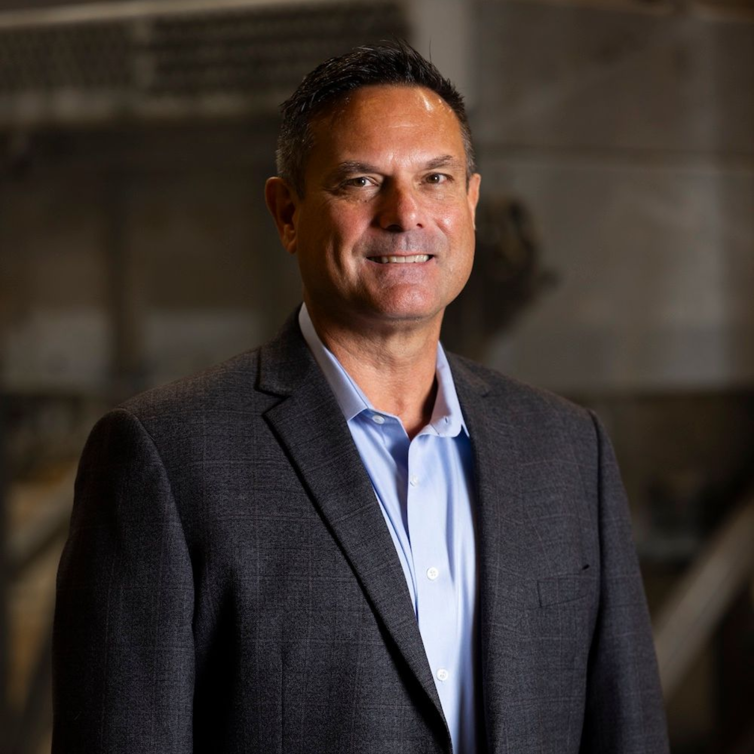 Man in blazer and pink shirt, smiling with a beard, indoors.