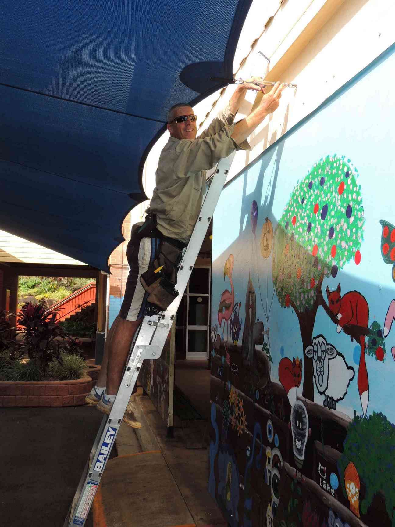 A Man On A Ladder Painting A Mural On A Wall — Style Shades Installation In Edmonton, QLD