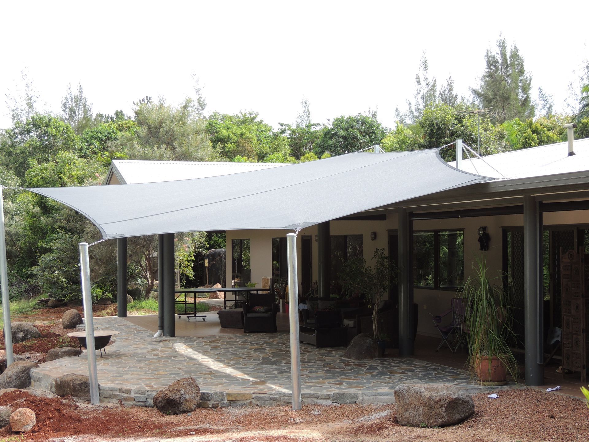 A Large Gray Shade Sail Is Covering A Patio Area In Front Of A House — Style Shades Installation In Mareeba, QLD