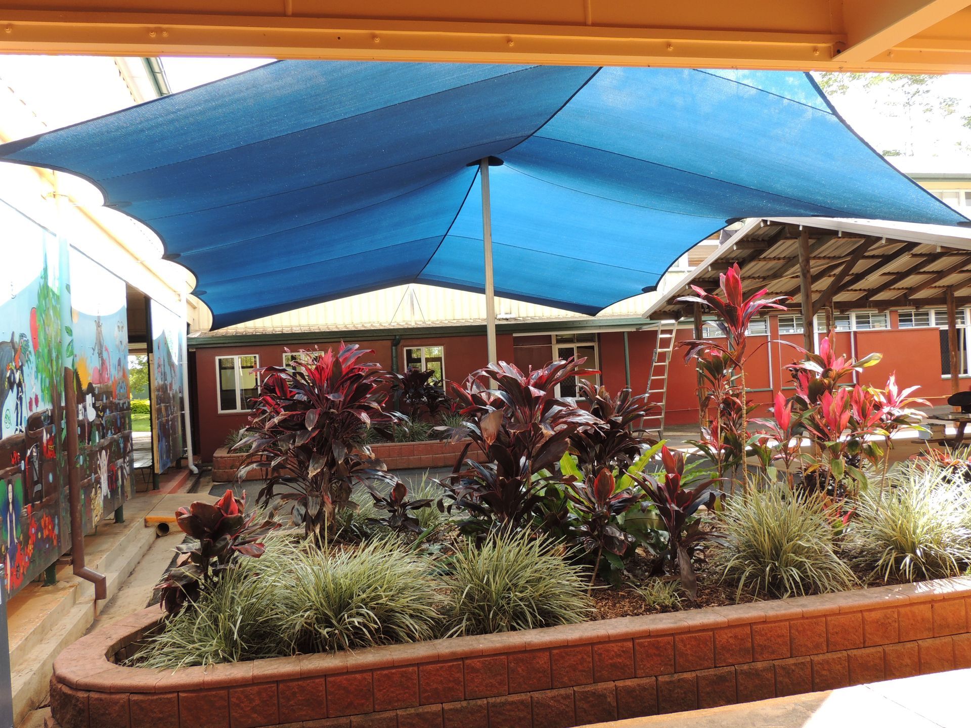 A Blue Umbrella Is Hanging Over A Garden With Lots Of Plants — Style Shades Installation In Edmonton, QLD
