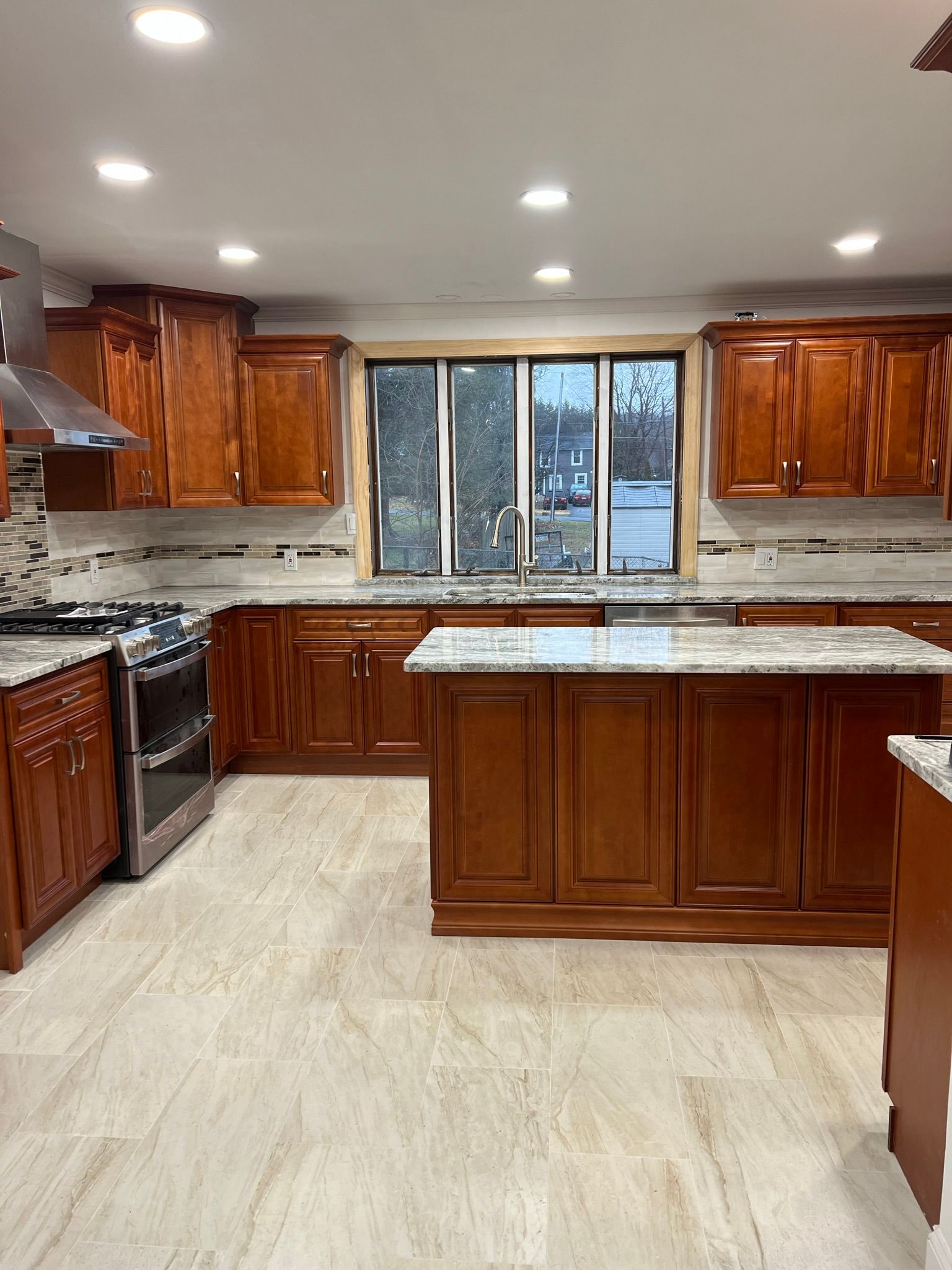A kitchen with wooden cabinets , granite counter tops , a stove , and a large island.