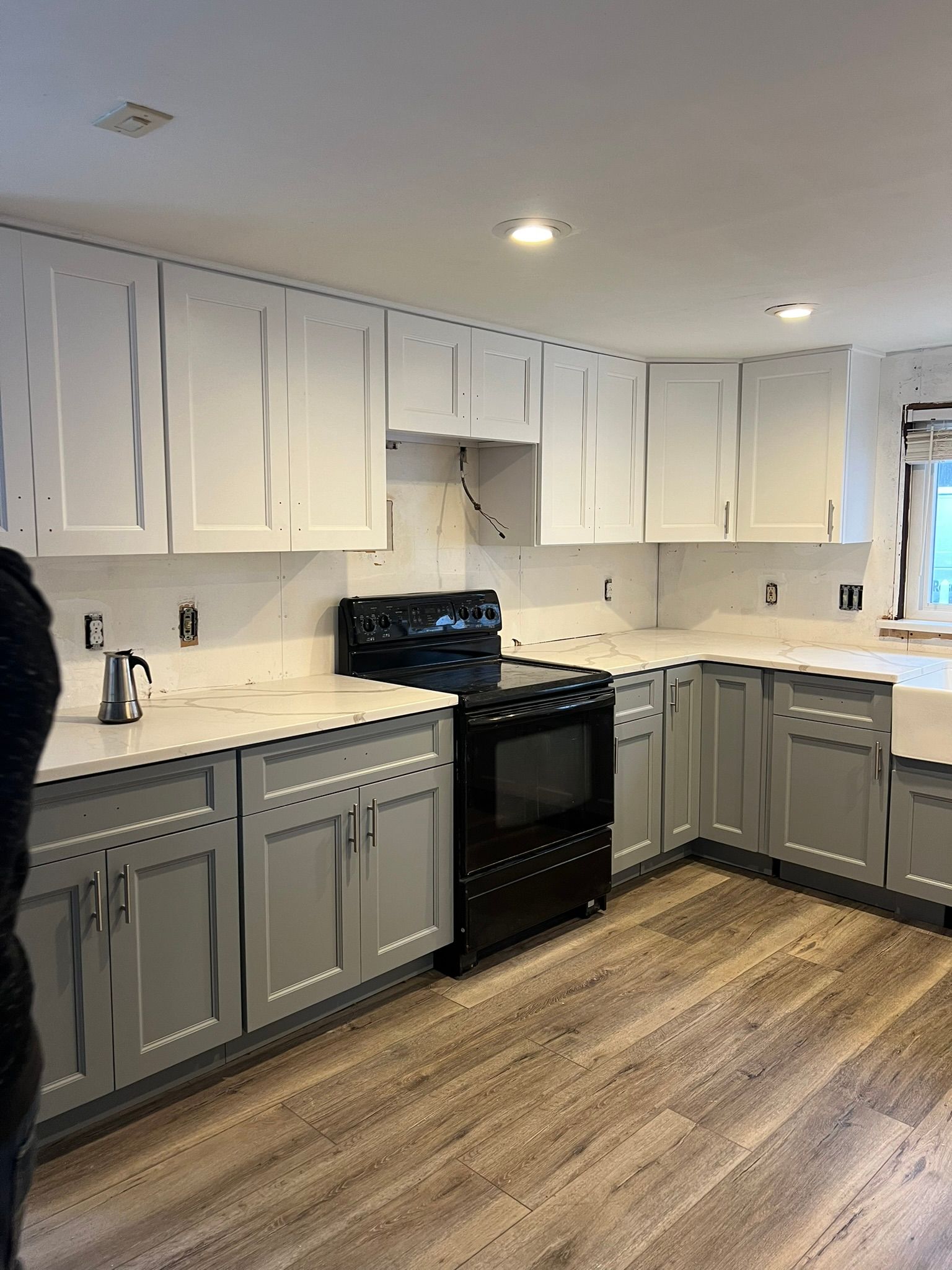 A kitchen with gray cabinets , white counter tops , and a black stove.