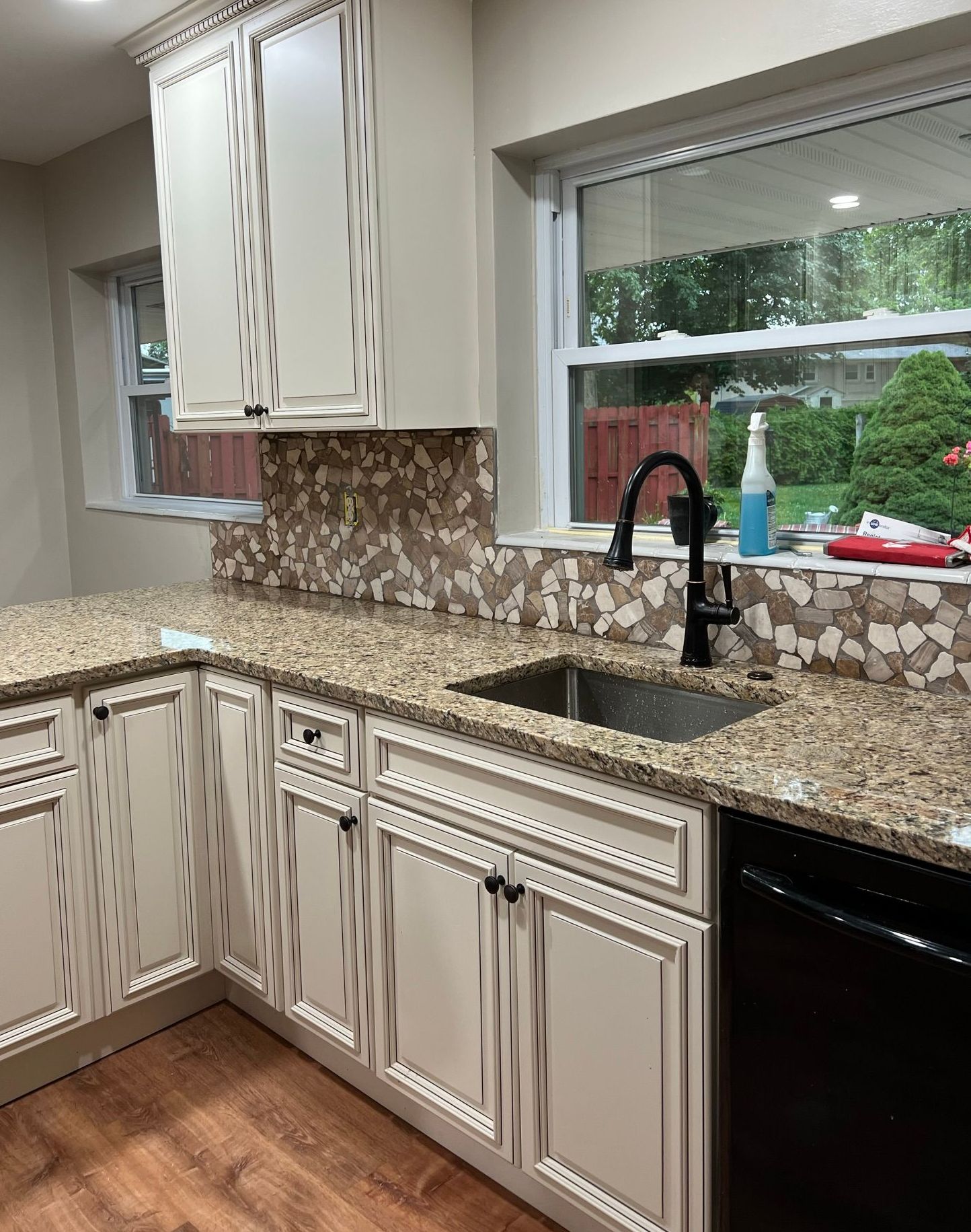 A kitchen with white cabinets , granite counter tops , a sink and a window.