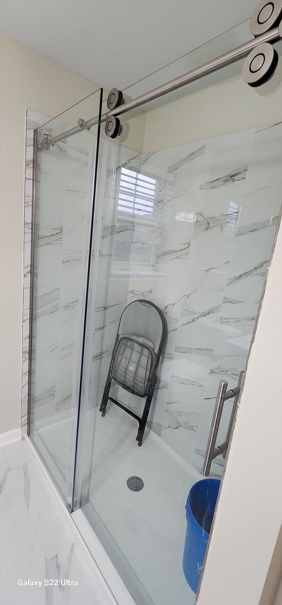 A bathroom with a sliding glass shower door and a chair in the shower.