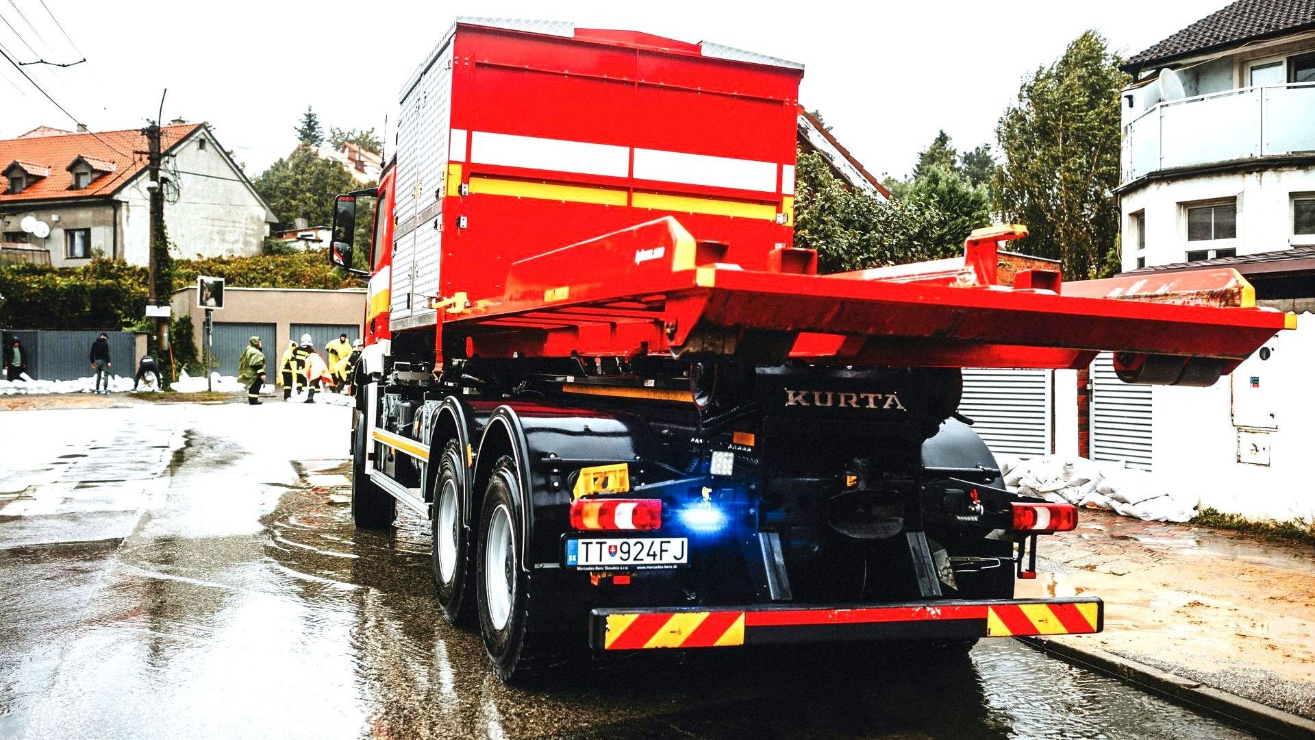 A red truck is driving down a wet street