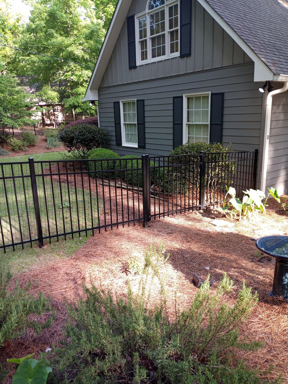 A gray house with black shutters and a black fence in front of it.