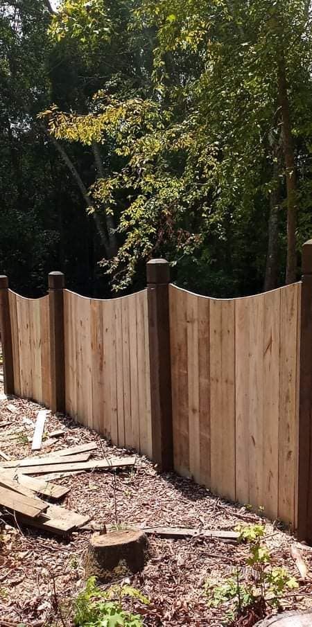 A wooden fence is surrounded by trees in a backyard.