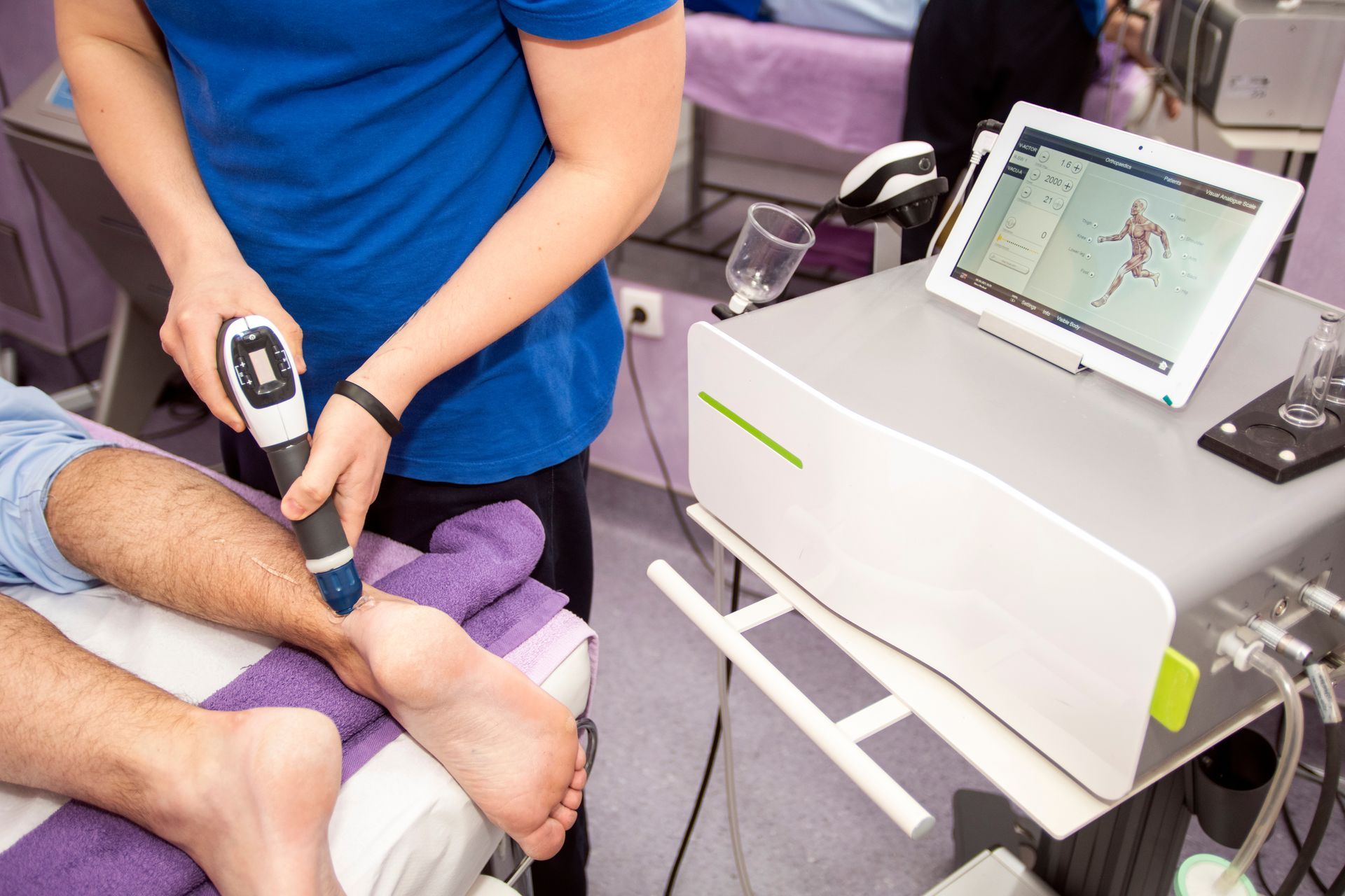 Eine Frau behandelt den Fuß eines Patienten mit Stosswellentherapie