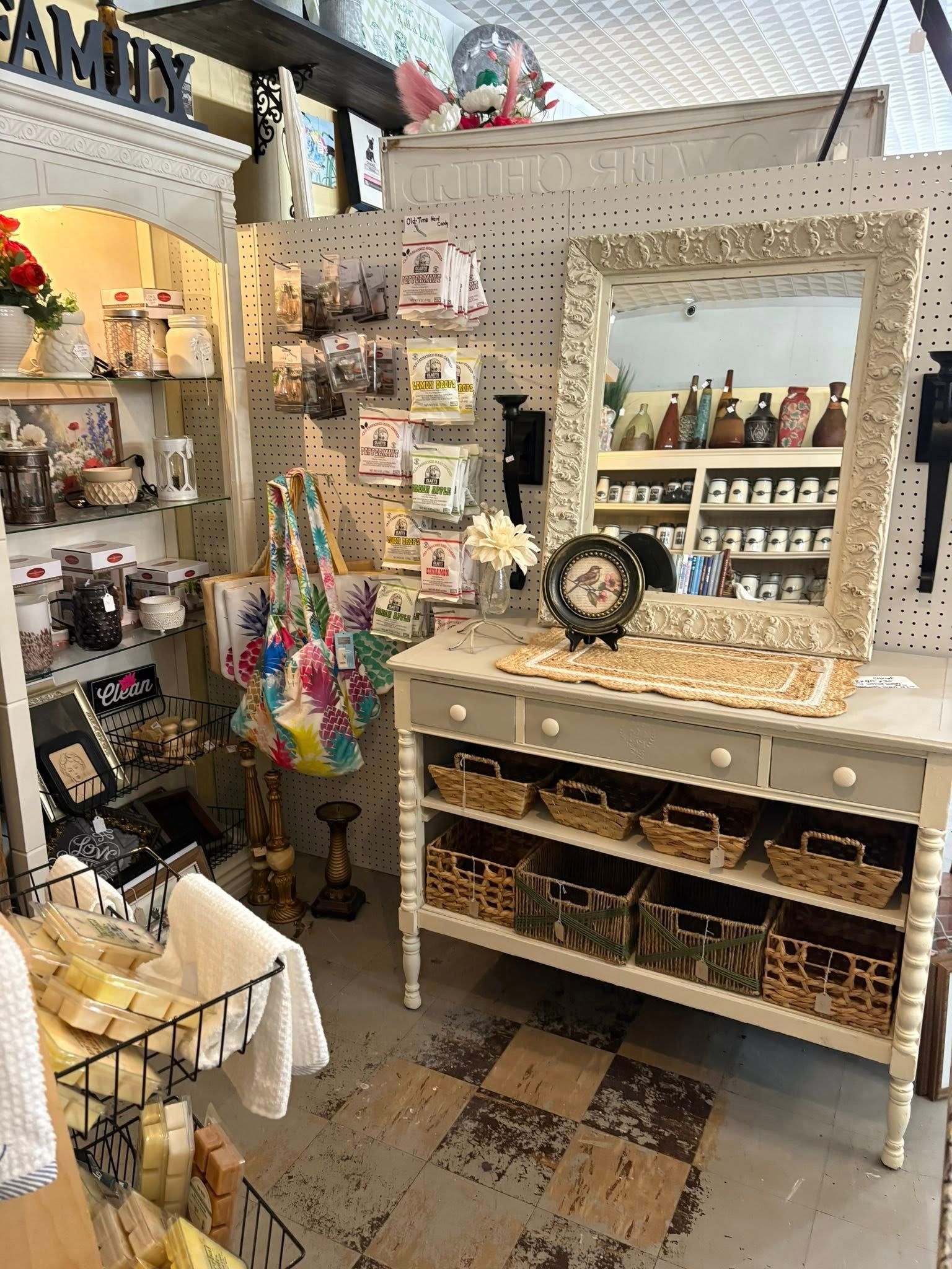 Eclectic shop interior with white shelves, decorative items, and a large mirror above a display table.