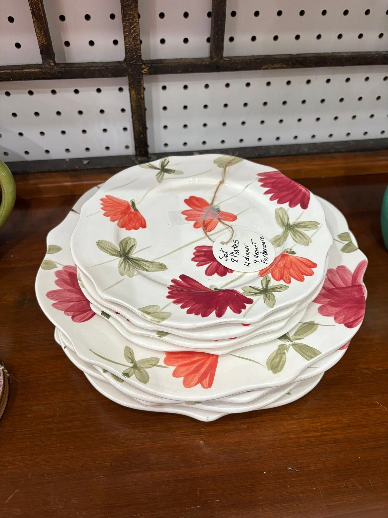 Stacked floral-pattern plates on a wooden table in front of a pegboard wall